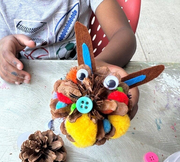 Close up on a child's art project made from pinecones, felt, and googly eyes.