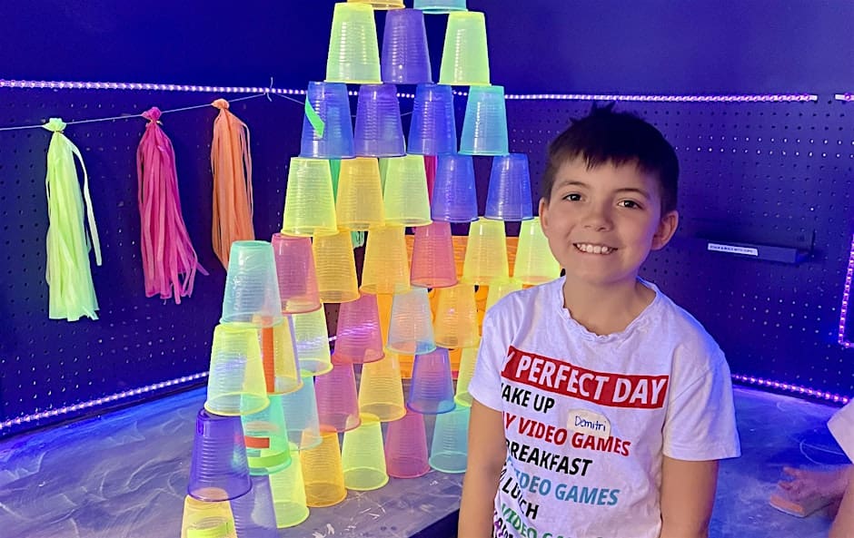 A kid with glowing drinking cups under a blacklight.