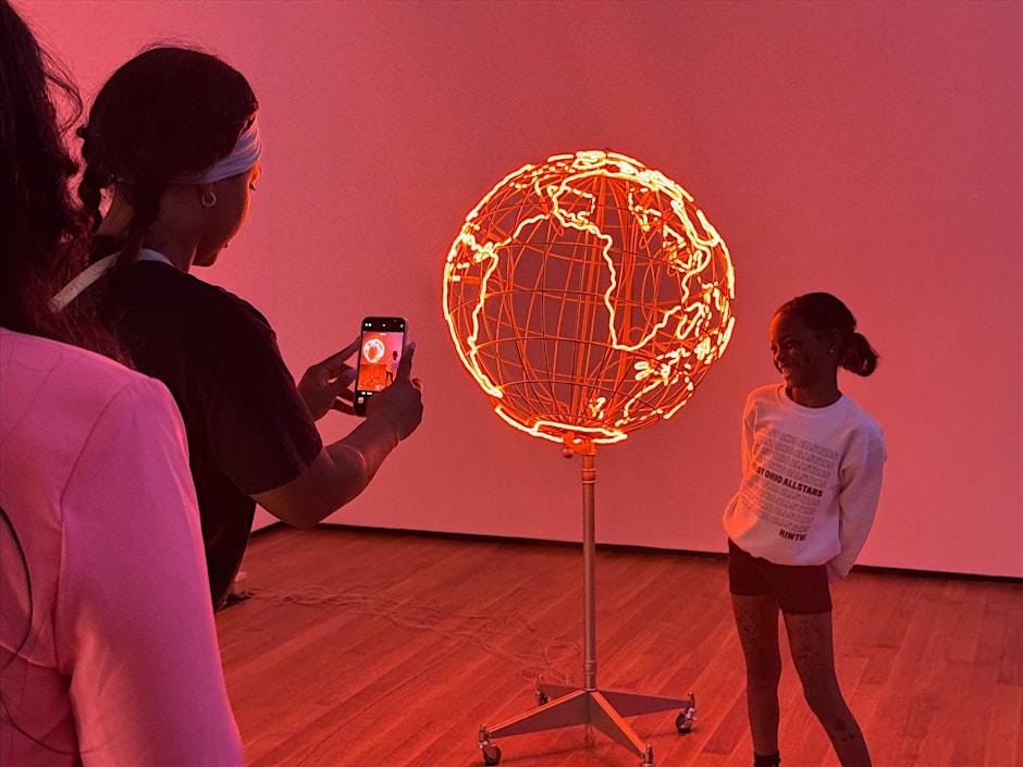 A young girl getting her pictures taken by an artwork.